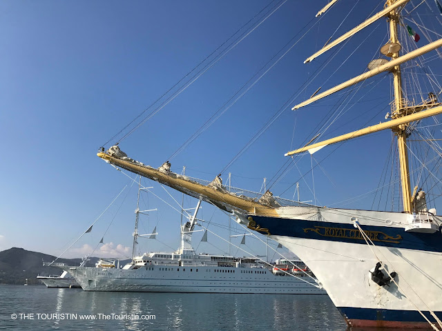 A tall ship next to a cruise ship under a bright blue sky.