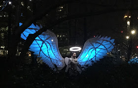 Pic of lady standing under the halo of the artwork with angel wings lit in blue