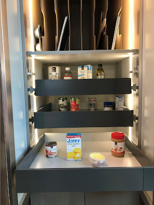 An accessible cupboard is shown. Three retractable shelves are shown, the bottom of which is pulled out. Each drawer holds a variety of condiments or canned foods