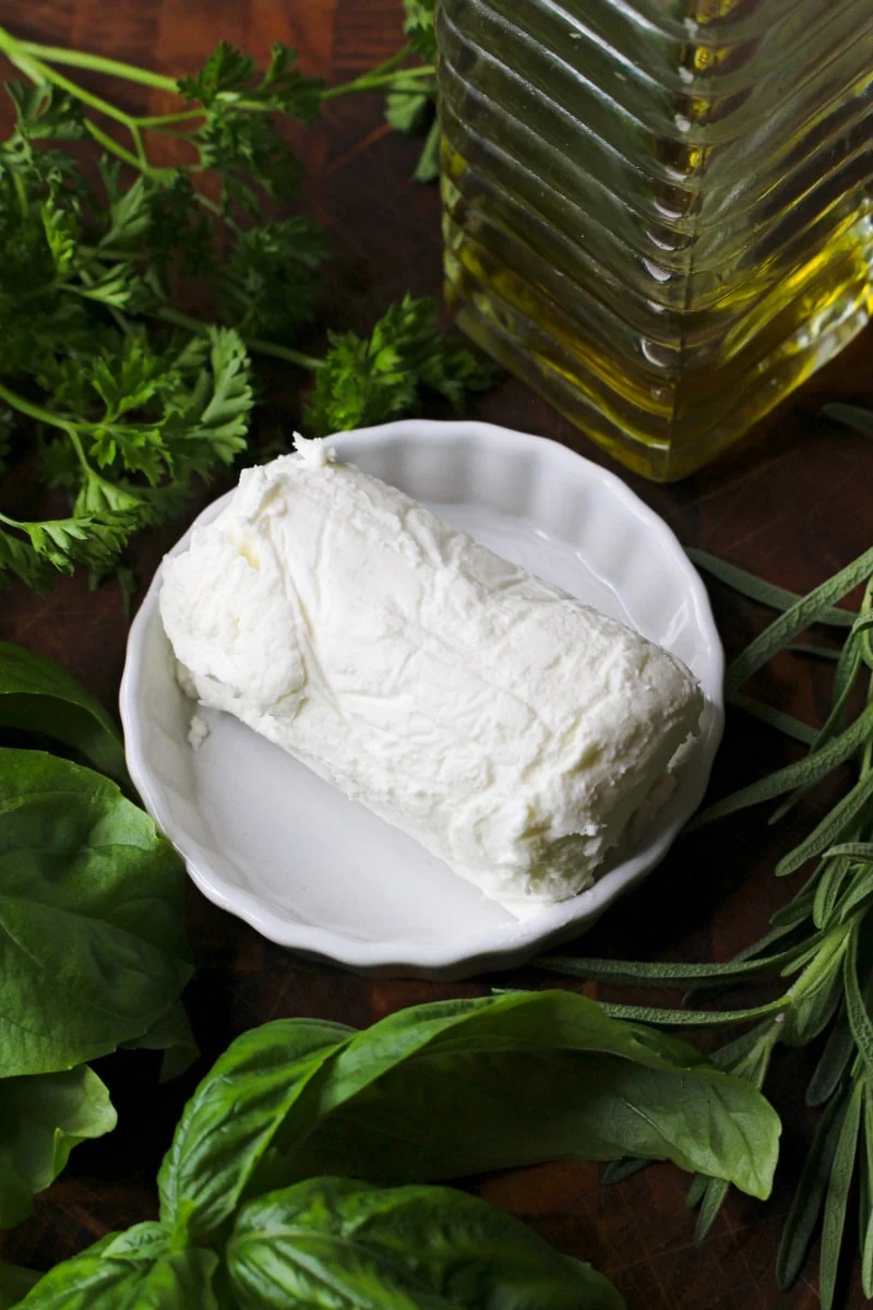 Top view Herb and Olive Oil Goat Cheese Log ingredients on a wood cutting board.