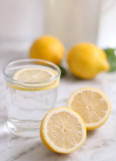 A glass of water with a slice of lemon in it, whole lemons in the background
