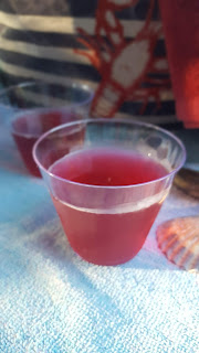 a cup of grape juice mixed with lemonade on a beach towel with a beach bag