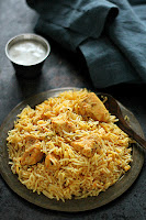 Hyderabadi Boneless Chicken Biryani in a metal plate beside a bowl of raita.