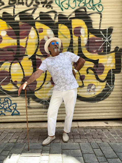 Man with cane posing against a grafitti'd wall