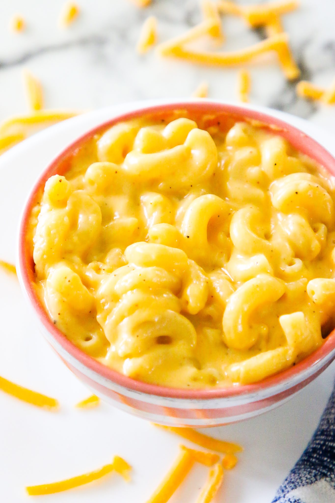 A small bowl of mac n cheese on a white plate with a blue towel in the background.