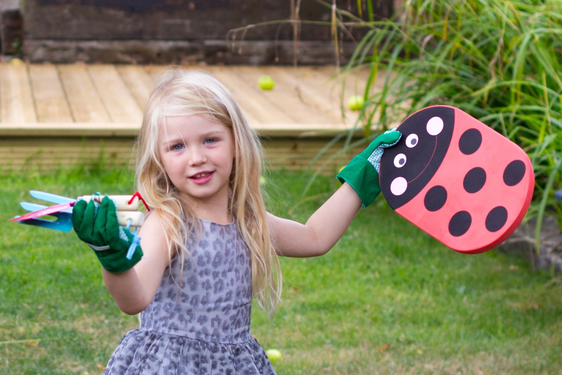 A young child holding gardening gloves and tools