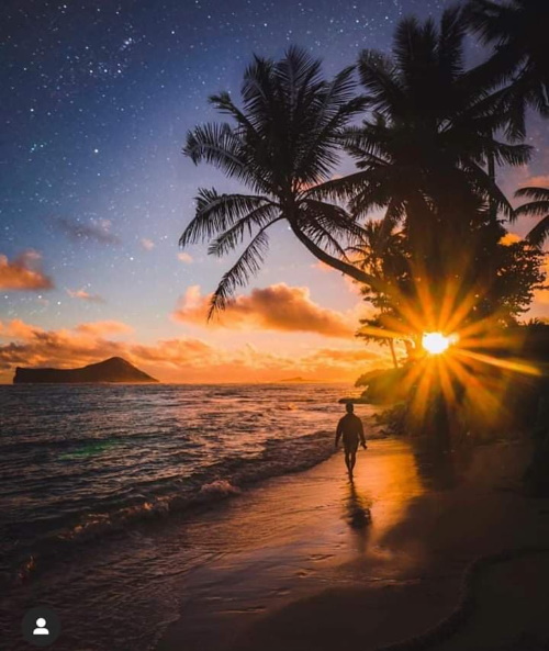 Linda paisagem do sol iluminando a água do mar e um jovem caminhando na areia.