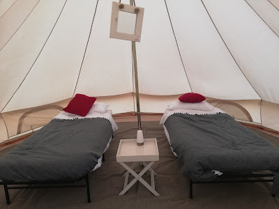 inside a bell tent, allneat and tidy, two beds with a red pillow on each and a small table