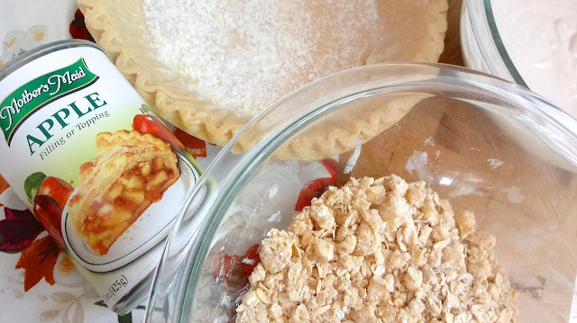 a can of apple pie filling sitting next to a frozen pie crust and a bowl of crumble