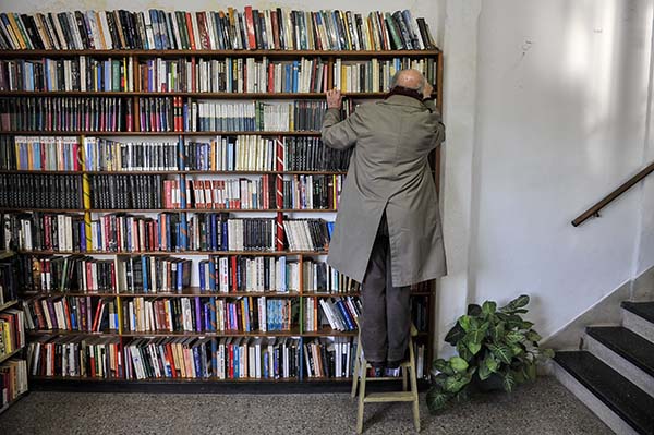 hombre mayor subido a una escalera buscando un libro en una biblioteca personal grande