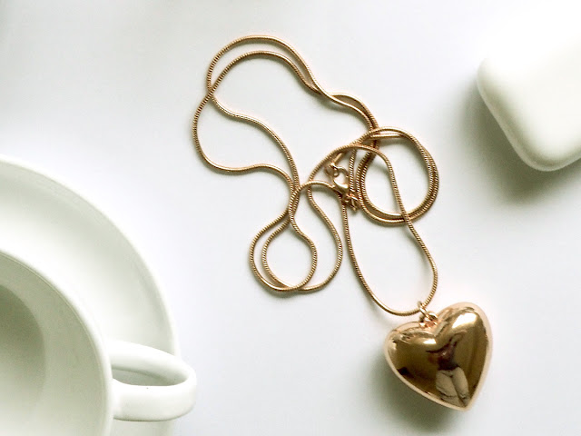 Gold necklace with a heart pendant display on top of a white table