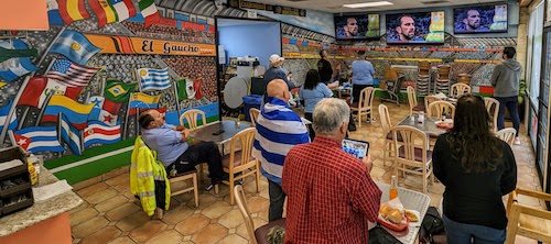 Fans stand for and sing the national anthem of Uruguay, surrounded by the stadium painting in the dining room