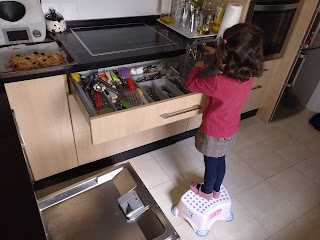 Mi niña de espaldas sacando los cubiertos del lavavajillas y poniéndolos en el cajón. 