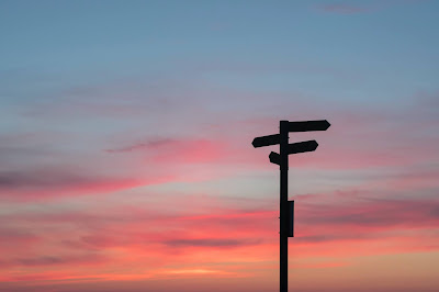 En bild som visar vägskyltar mot himmel flerfärgad himmel i solnedgångsfärger.