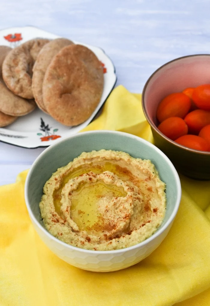 homemade hummus in a blue and white bowl on a yellow linen napkin