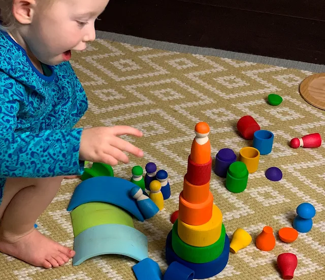 Toddler building a tower with colourful Grimms wooden pieces