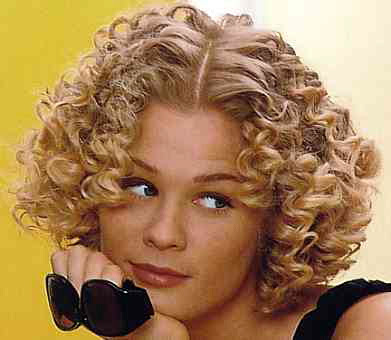The model has short to medium, curly hair in a curly bob style with a fringe 