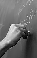 Foto en blanco y negro de un maestro escribiendo en un pizarrón