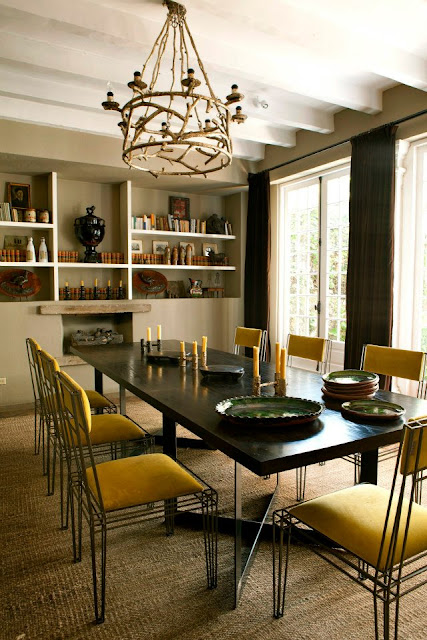 dining room from casamid facebook with yellow chairs, a fireplace, built in bookshelves full of books and small sculptures, floor length curtains, french doors and a wood chandelier light