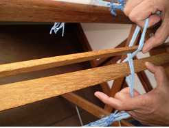 Foto mostrando como colocar as duas réguas entre os fios da “cruzada” para preparar os fios do urdume para serem colocados no tear.