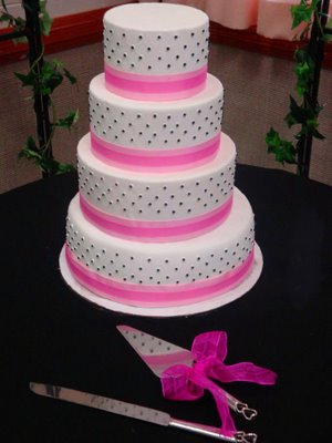 Black polka dots over a white fondant four tier cake with bright pink ribbon