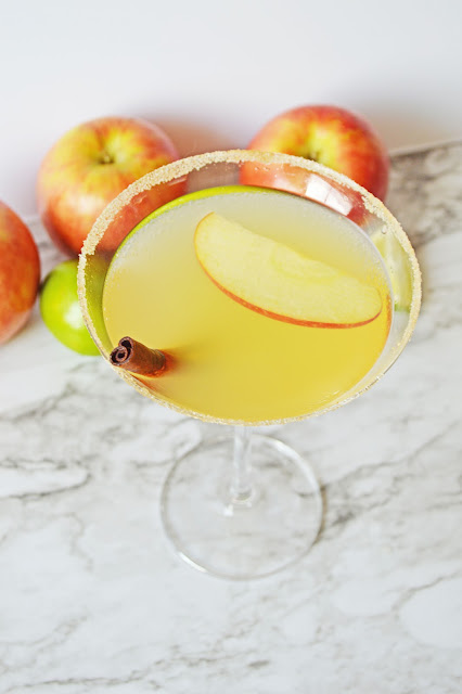 martini in a clear glass with gray background and cinnamon and apple garnish.