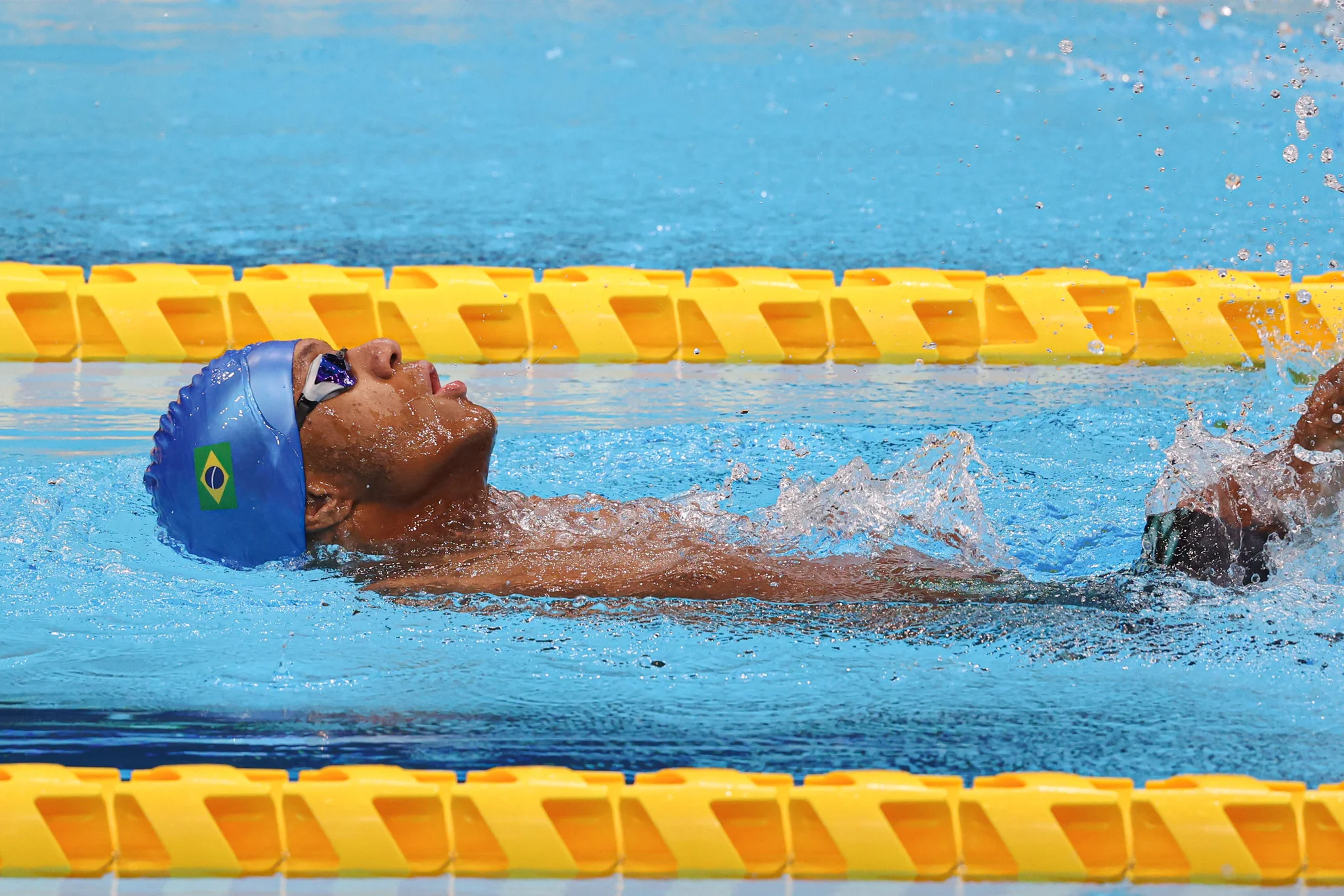 Usando uma touca azul, Gabriel Araújo nada de costas no meio das raias amarelas