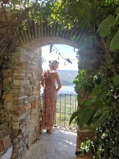 Aline in a red dress on a balocne watching the view, broad walls, climbing plants around