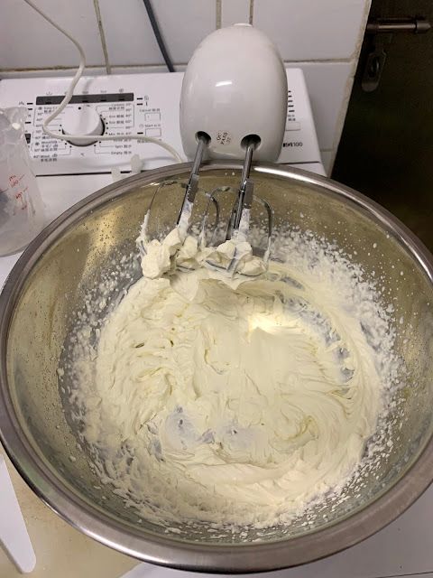 Metal bowl of whipped cream and hand mixer
