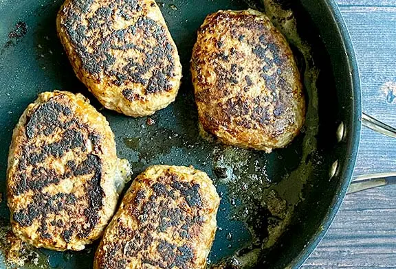 Salisbury steaks frying in a pan.