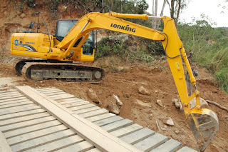 Na entrada para a Granja Mafra, com o auxílio de uma escavadeira, profissionais da Prefeitura trocam uma ponte de lugar