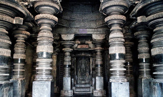 10 of the 12 elegantly carved pillars of the navaranga, Parshvanatha statue at the center, and the ceiling sculptures partially visible through the door.