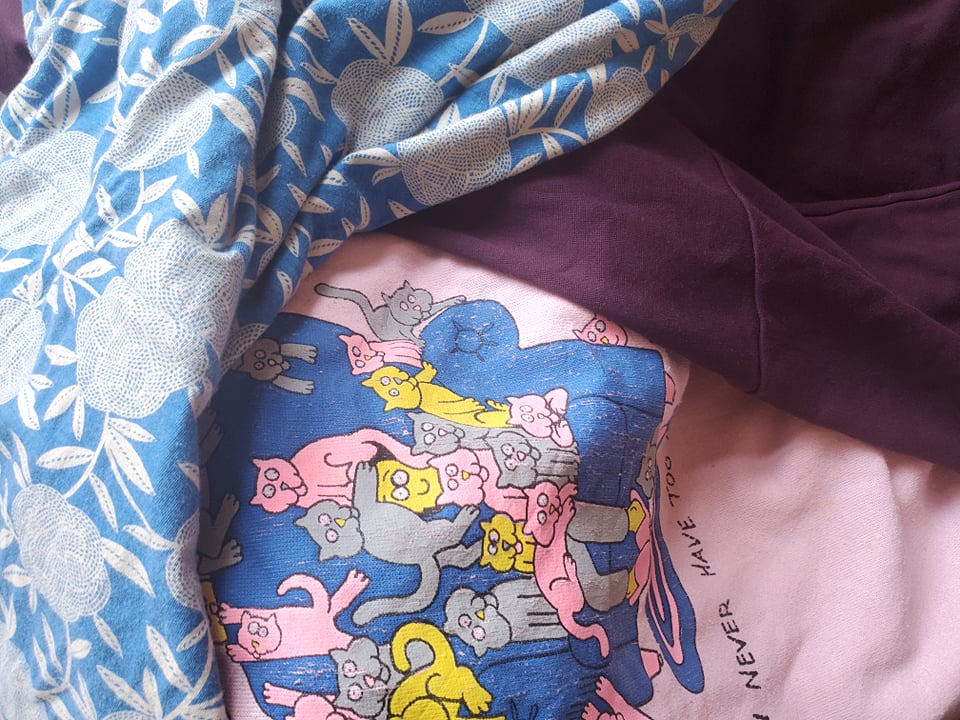 secondhand clothes including blue print dress, pink cat design crew neck jumper, and purple skirt