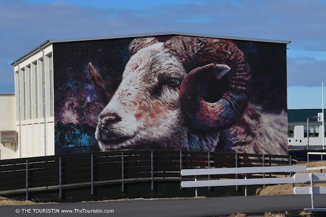 Purple and blue, black mural of a white ram on the facade of a house.