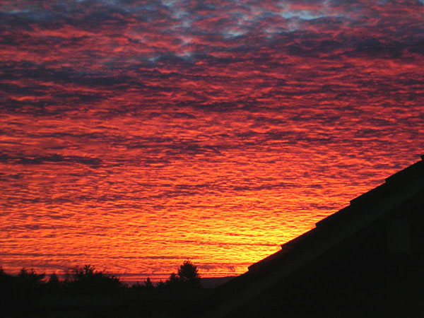 sky dappled with red clouds over the silhouette of a roof