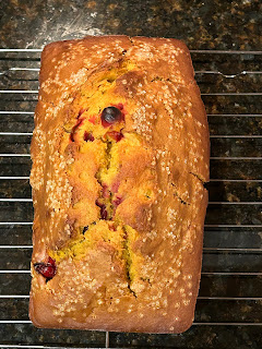 A baked, golden pumpkin-cranberry bread on a metal cooling rack.