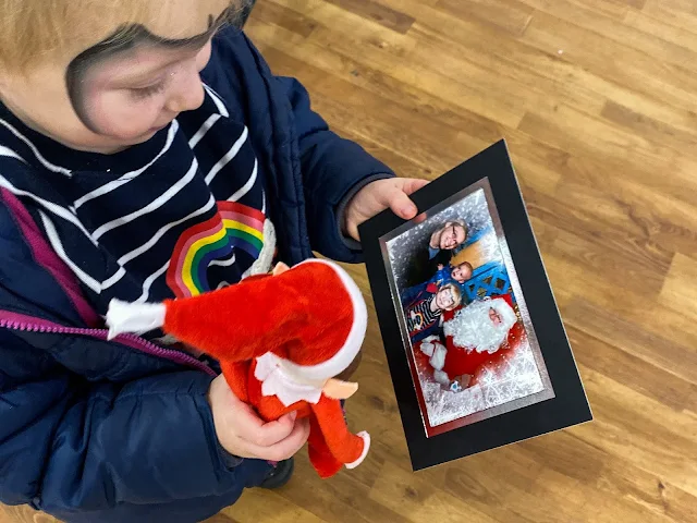 Overhead shot of a girl with an elf toy from Santa looking at a photo of her with Father Christmas