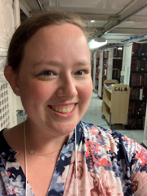 A smiling woman takes a selfie with shelves of books in the background