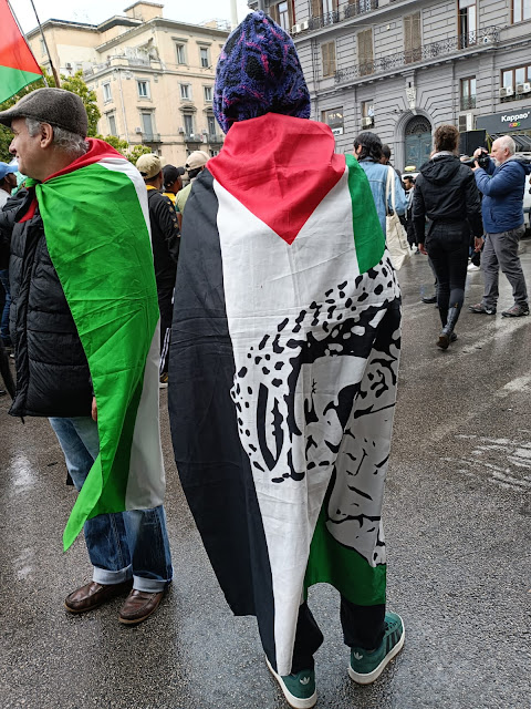 Persona di spalle ricoperta da una bandiera palestinese con il volto di Arafat