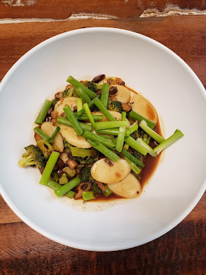 a bowl with Korean rice cakes, mushrooms, broccoli, and green onions in a spicy sauce