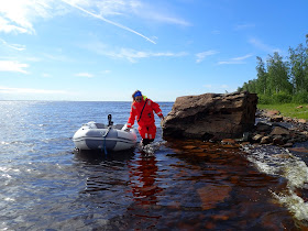 Pelastautumispukuinen henkilö vetää kumivenettä matalassa rantavedessä. 