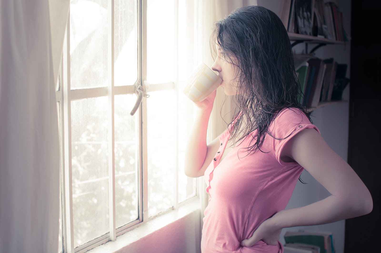 朝の窓辺で立って珈琲を飲んでいる女性