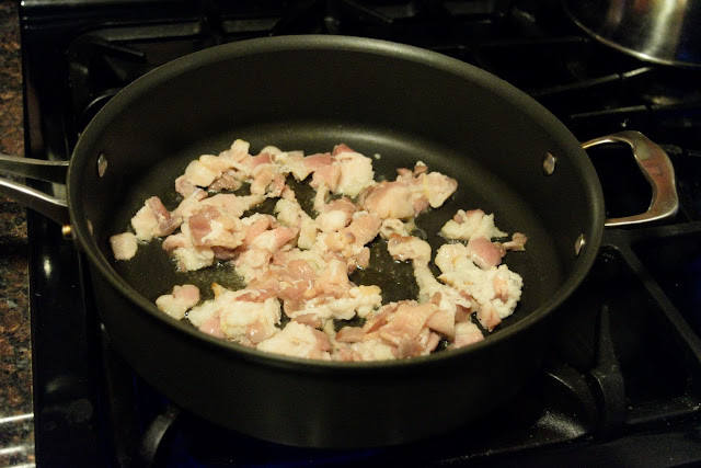 The sliced bacon rendering down and crisping in a skillet. 