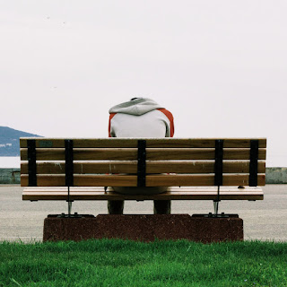 A sad, dejected teen sitting on a bench, head down.