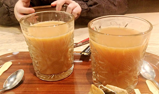 Two glass tumblers containing tea, on a tray with spoons and used teabags. 
