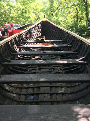 A view down the center of a Viking longship with broad benches spanning the interior and dappled sunlight falling on the stern.