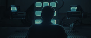 silhouette of person sitting in front of a bank of tv screens showing white noise