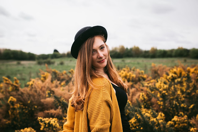 woman standing in front of yellow flowers in bowler hat and looking at the camera posing