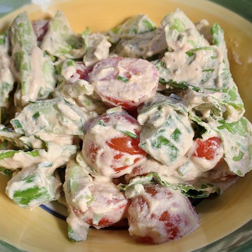 Close up of bowl of Salad with cucumbers, lettuce and cherry tomatoes. Tossed in creamy vegan hazelnut miso dressing.