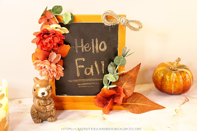 Completed craft, framed chalkboard with faux floral and leaves displayed near squirrel figurine and mini pumpkin